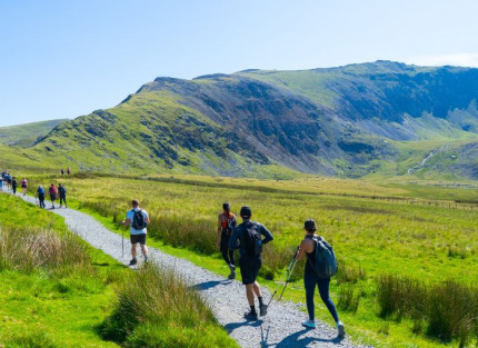 A large group of hikers walking along a mountain path on a sunny day